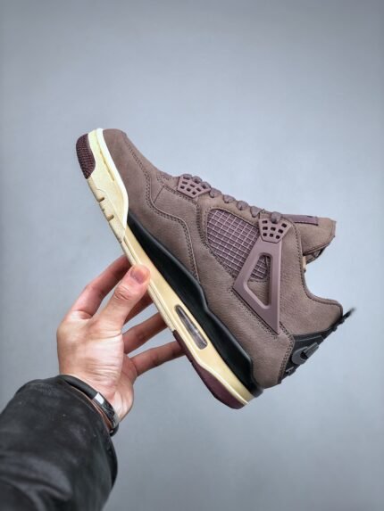 A hand holding a brown sneaker, showing the sole and upper details