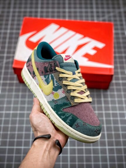 A hand holding a green and yellow Nike Dunk Low sneaker with a red Nike shoebox in the background.
