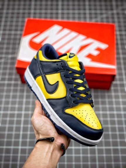 A pair of yellow and black Nike Dunk Low sneakers placed on a grid surface.