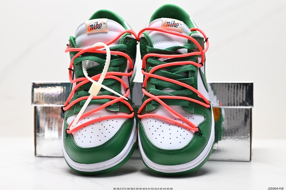 A pair of green and white Nike Dunk Low sneakers with orange laces, placed in front of a shoebox.