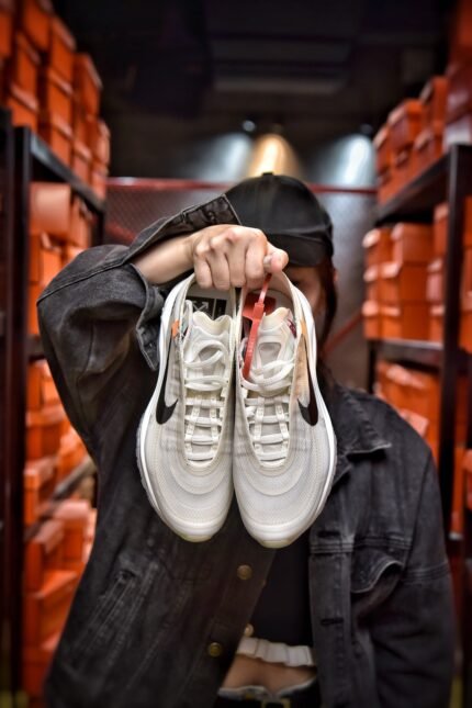 A pair of white sports shoes with black details, displayed by a person in a denim jacket