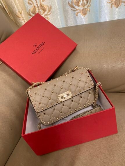 Beige studded handbag in a red box, with a beige sofa in the background