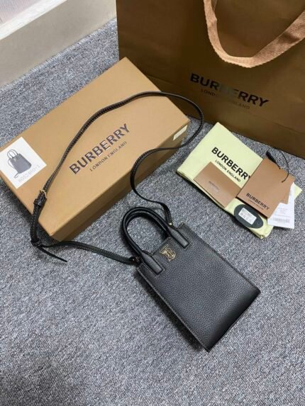 A black leather handbag with a detachable shoulder strap, placed next to a cardboard box and packaging materials.