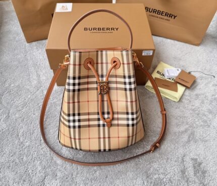 A beige check-patterned handbag with brown leather straps and a gold-tone buckle, placed next to a cardboard box.