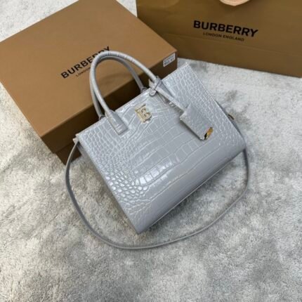 A light gray crocodile-textured handbag with handles and a detachable shoulder strap, next to a cardboard box.