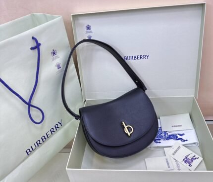 A dark blue leather handbag with a gold metal clasp in an open gift box.