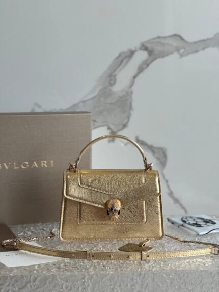 A gold handbag with a snake head clasp and chain strap.