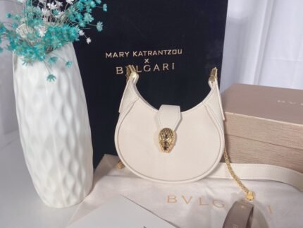 A white handbag with a gold metal clasp and chain shoulder strap, with a white vase and blue flowers in the background.