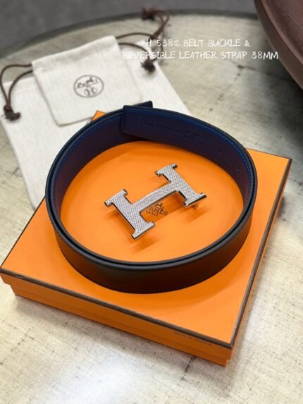 This is a reversible leather belt with a silver metal buckle, displayed on the brand's elegant packaging.