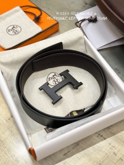 This is a reversible leather belt with a black metal buckle, displayed on the brand's elegant packaging.