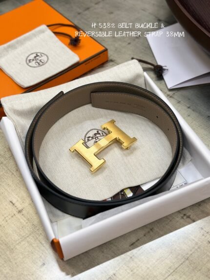 This is a reversible leather belt with a gold metal buckle, displayed on the brand's elegant packaging.