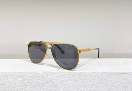 Gold metal-framed sunglasses with dark lenses, placed on a white surface against a white wall.