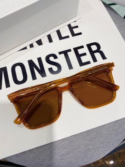 A pair of stylish amber-colored Gentle Monster sunglasses placed on a white box with the brand name "Gentle Monster" printed on it.