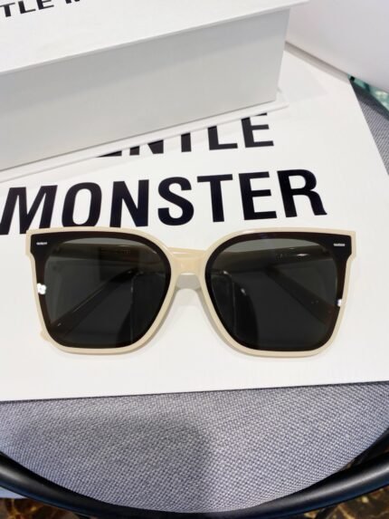 A pair of stylish Gentle Monster sunglasses with a white frame and dark lenses, placed on a white box with the brand name "GENTLE MONSTER" printed on it.