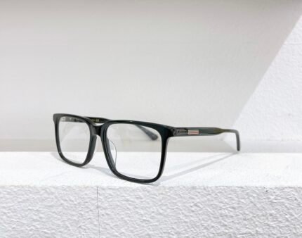Black Gucci optical glasses with clear lenses, placed on a white surface against a white wall.