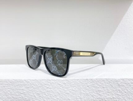 Black Gucci sunglasses with white "GG" logo on the lenses, placed on a white surface against a white wall.