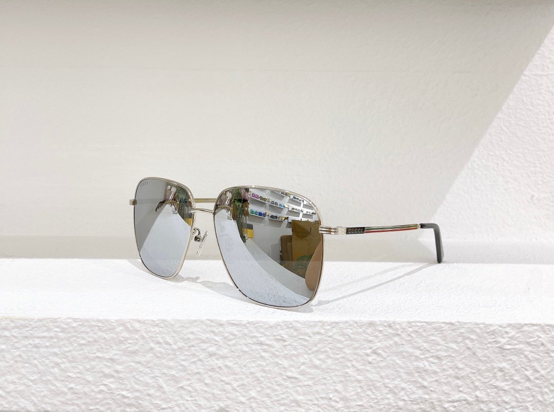 Stylish Gucci Sunglasses with Reflective Lenses A pair of silver metal-framed Gucci sunglasses with reflective lenses, placed on a white surface against a white wall.