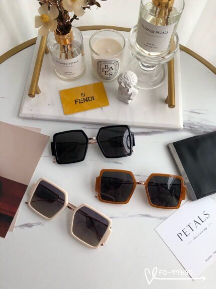 The image features a stylish arrangement of Fendi sunglasses displayed on a marble surface. There are three pairs of sunglasses in different colors: black, white, and brown. In the background, there are decorative items such as a vase with flowers, a candle, and a Fendi branded card, creating an elegant and luxurious atmosphere.