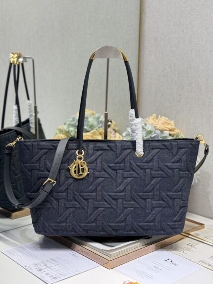 Dark blue woven texture tote bag with gold charm, comes with a long shoulder strap, against a backdrop of brand books and packaging