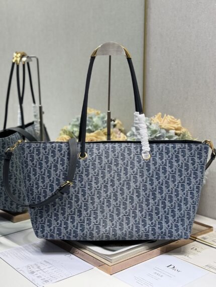 Blue patterned tote bag with black straps, gold hardware, against a backdrop of brand books and packaging