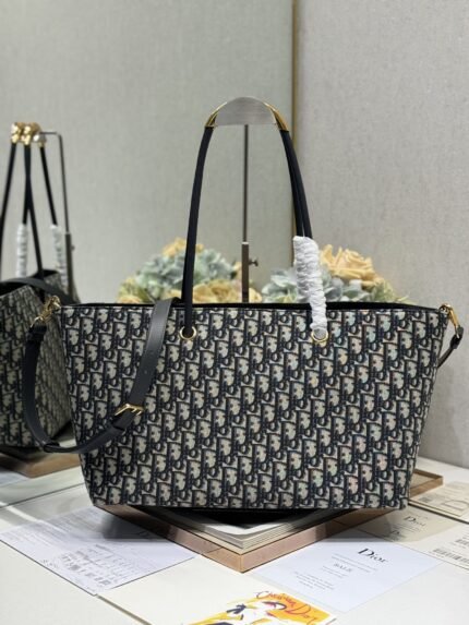 Blue and white patterned tote bag with black straps, gold hardware, against a backdrop of brand books and packaging