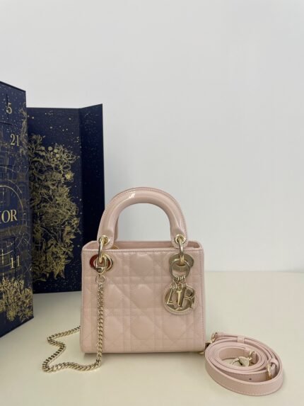 Pink patent leather quilted handbag with gold chain and charm, comes with a long shoulder strap, against a decorative box background
