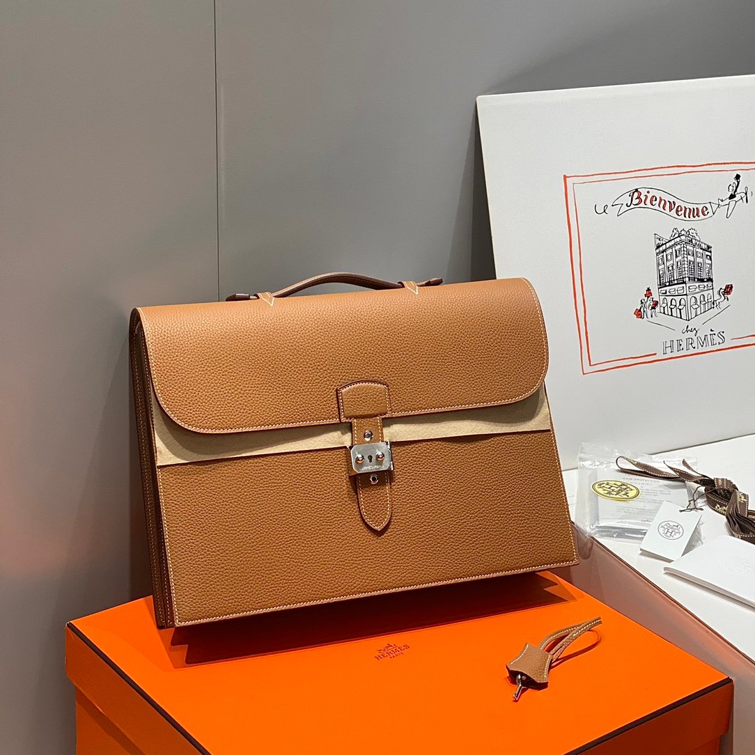 Tan leather handbag with silver metal buckle, displayed on an orange box