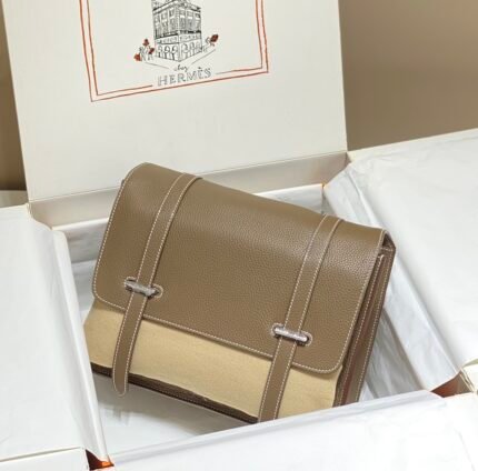 Brown leather handbag with silver metal buckles, placed in a white box