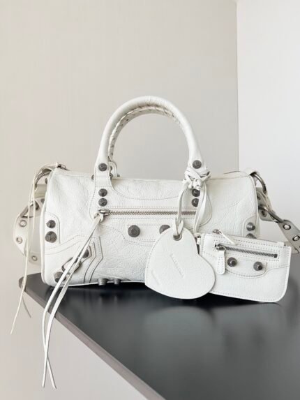 White handbag with multiple zippers and metal buckles, next to a heart-shaped pendant and a small wallet.