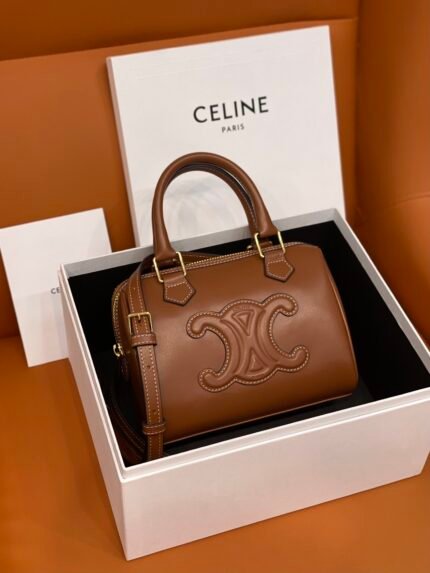 Brown leather handbag with gold accents, inside a branded packaging box