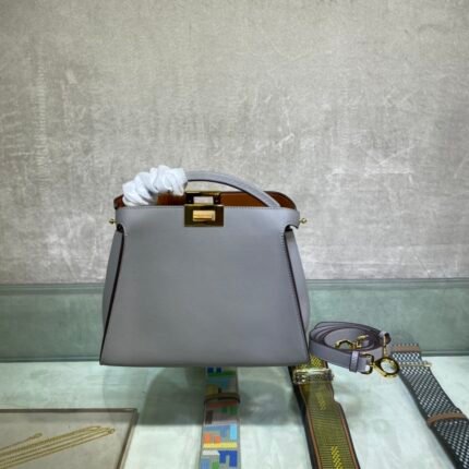 Grey handbag with gold lock, comes with multicolor strap, on a marble background